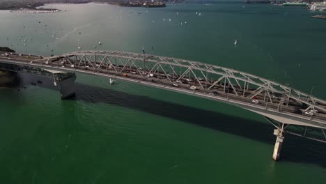 Vehículos-Que-Cruzan-El-Puerto-De-Waitemata-A-Través-Del-Puente-Del-Puerto-De-Auckland-En-Auckland,-Nueva-Zelanda-Con-Barcos-A-La-Deriva-En-Aguas-Turquesas