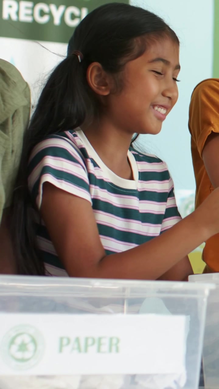 Vertical video: Reaching striped girl sorting into PAPER bin at school for recycling, boy resting