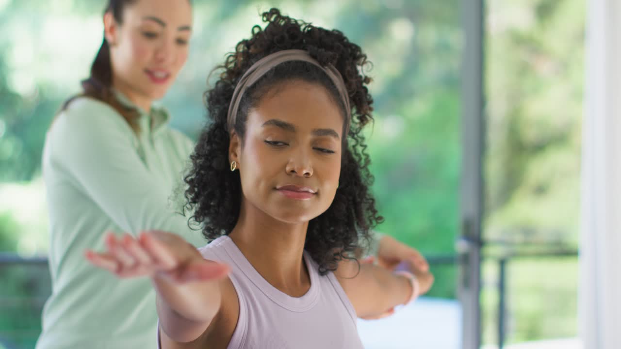 African American woman holding arm pose at home with headband after trainer cueing and fixing form