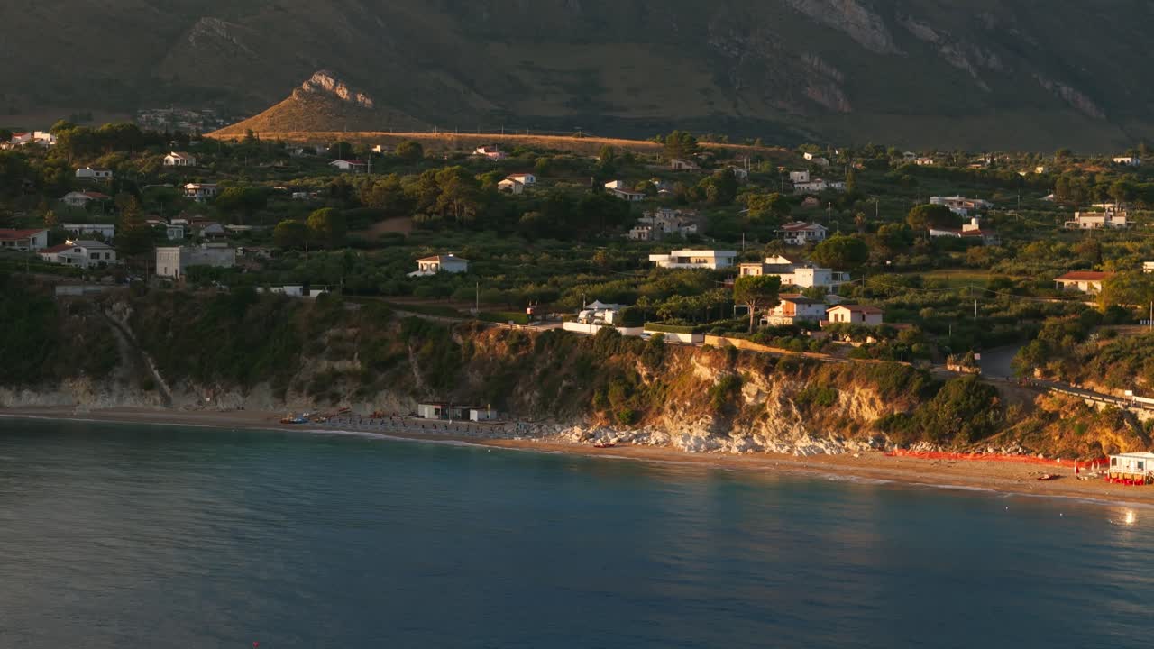 Aerial drone shot panning left over empty Guidaloca Beach during stunning golden sunrise in Sicily, Italy, showcasing serene coastal nature