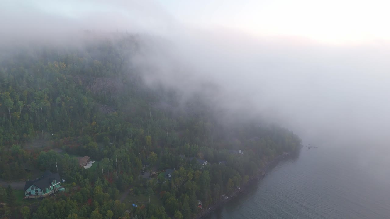 Morning fog drifts through an early autumn forest overlooking the vast waters of Lake Superior in Ontario, Canada. aerial view