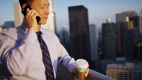 asian american businessman speaking on smartphone on rooftop