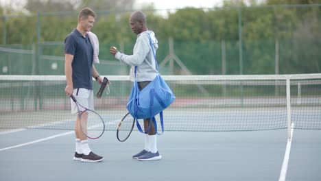 Happy-diverse-male-friends-looking-at-tennis-balls-and-talking-on-tennis-court,-slow-motion