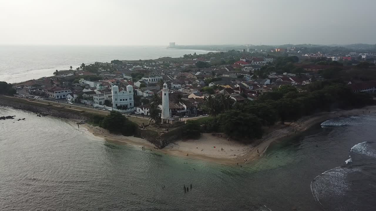 Flying over Galle's iconic lighthouse and beach, this drone shot shows the vibrant coastline and calm ocean waters stretching out as far as the eye can see.