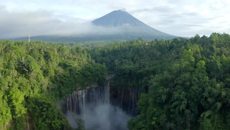 aerial view of a volcano sitting above a large exotic waterfall in a tropical rainforest at sunrise, east java indonesia