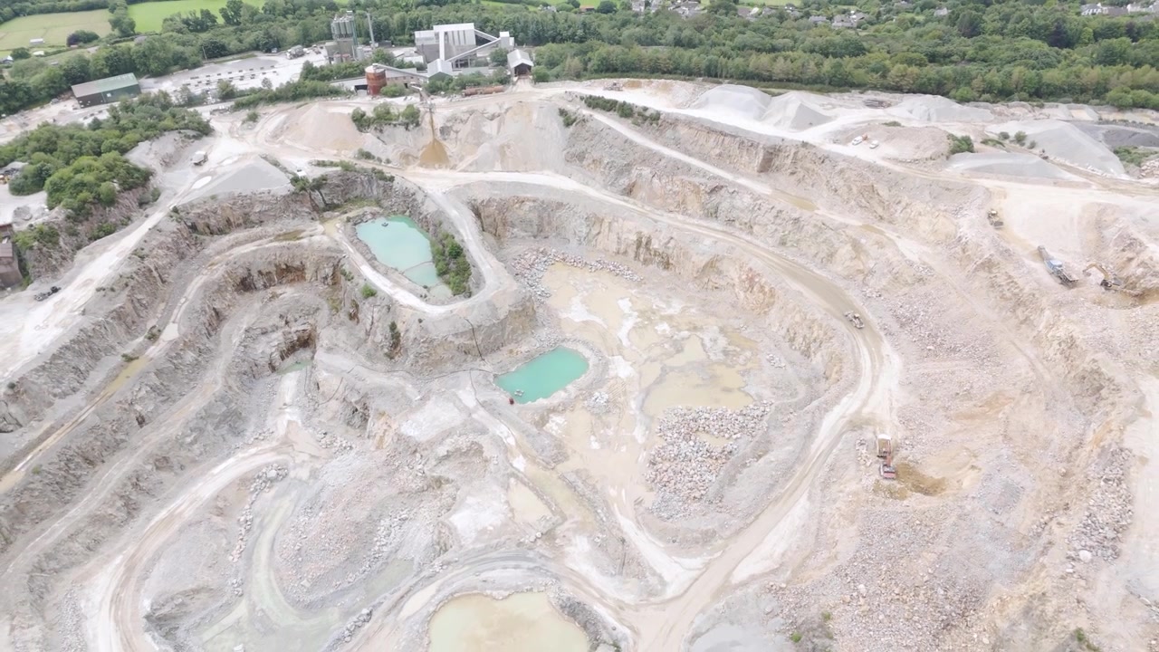 Aerial view of an active aggregate quarry with large pits and greenish water sumps, showcasing machinery at work