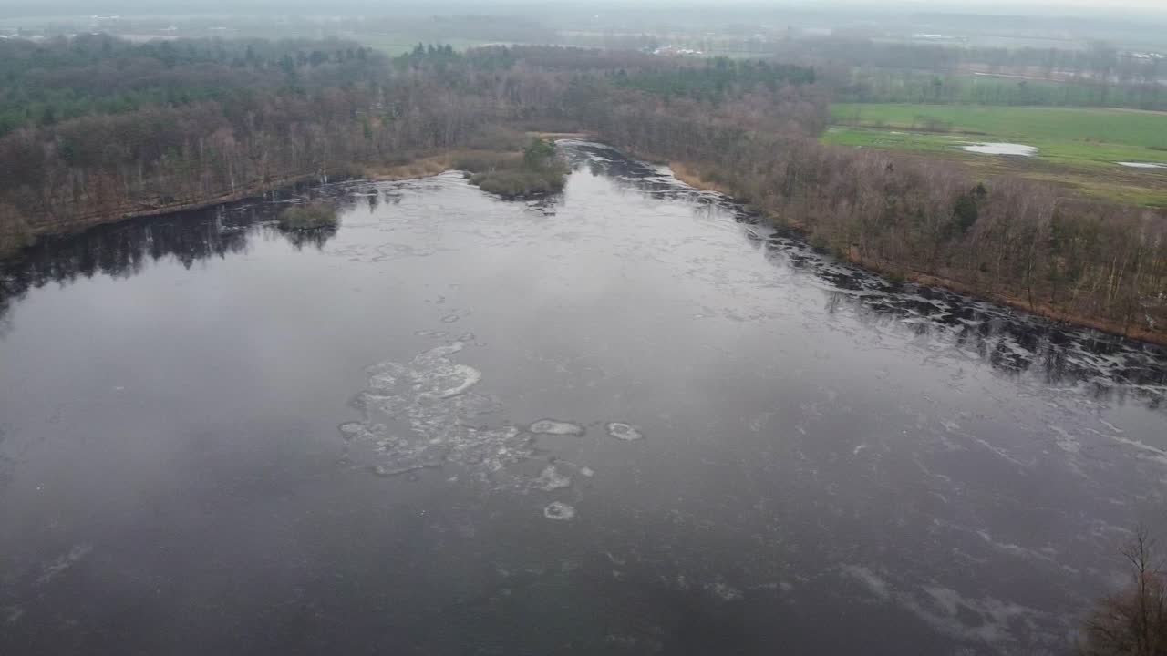 Luftfoto over isdækket sø i sneklædt vinterlandskab med skov i Retie, Belgien.
