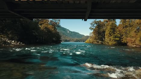 drone passes under a metal bridge very close to the water of a fast-flowing river