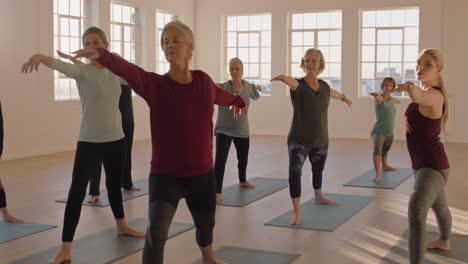 yoga class of healthy mature women practicing warrior pose enjoying morning physical fitness exercise workout in studio at sunrise