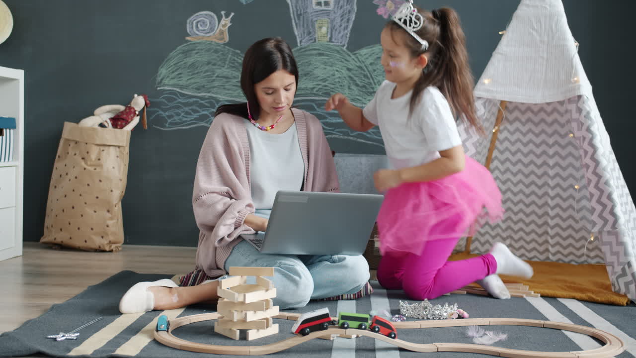 Mother working on laptop while daughter plays