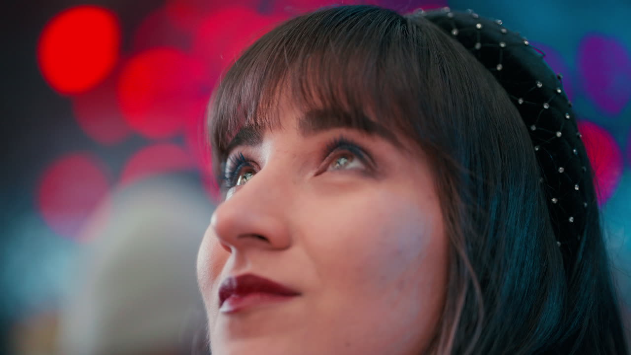 cerca de la cara de la mujer con cabello oscuro mirando hacia arriba rodeado de luces rojas bokeh en el ayuntamiento de viena rathaus mercado de navidad durante la noche en cámara lenta