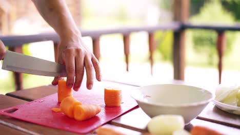 Close-up-Guy-is-cooking-pilaf-He-is-in-summer-house-cuts-carrots-on-a-red-cutting-board