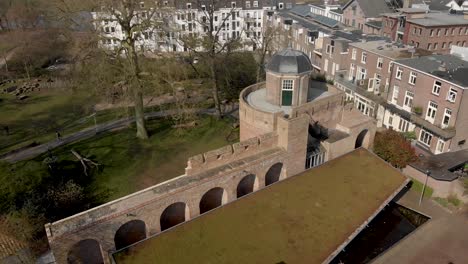 Sonniger-Tag-Langsame-Luftschwenkung-Mit-Spitze-Des-Historischen-Burgonje-festungsturms-Und-Der-Stadtmauer-Mit-Parklandschaft-In-Zutphen,-Niederlande