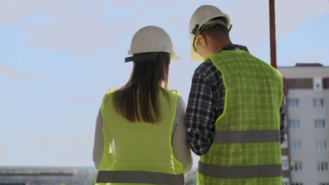 Pareja-De-Ingenieros-O-Técnicos,-Hombre-Y-Mujer-Con-Casco-De-Seguridad,-Sosteniendo-Un-Teléfono-De-Radio-Móvil,-Planificando-El-Plan-De-Construcción-Para-Saludar-El-Inicio-Del-Proyecto-En-El-Concepto-De-La-Industria-De-La-Construcción-En-El-Sitio-De-Construcción.