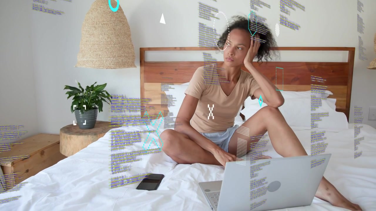 Adult woman on bed, leaning forward and typing, working from bed with laptop, phone, floating code