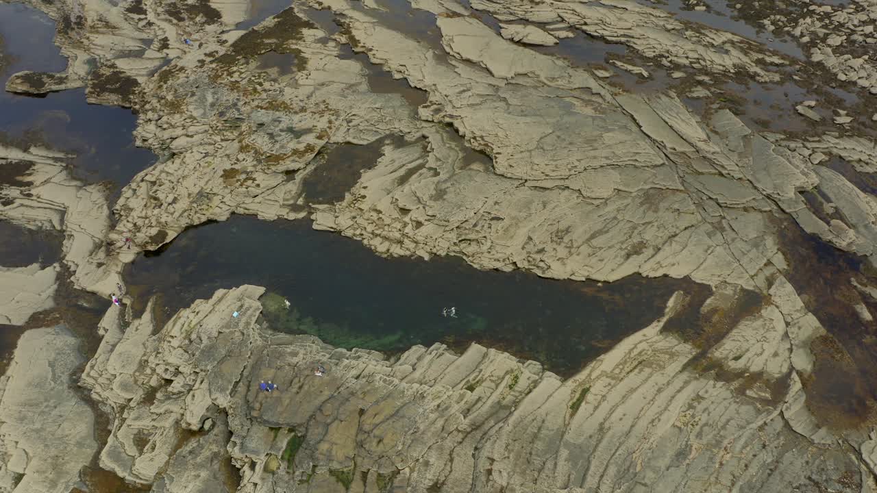 Aerial tilt up over Pollock Holes in Kilkee, capturing swimmers enjoying a refreshing dip