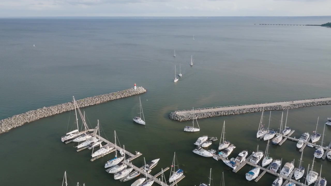 Un pequeño faro marca el final de un muelle rompeolas de piedra a lo largo del canal del puerto en Oakville. Veleros se mueven a través de la entrada hacia las aguas abiertas del lago