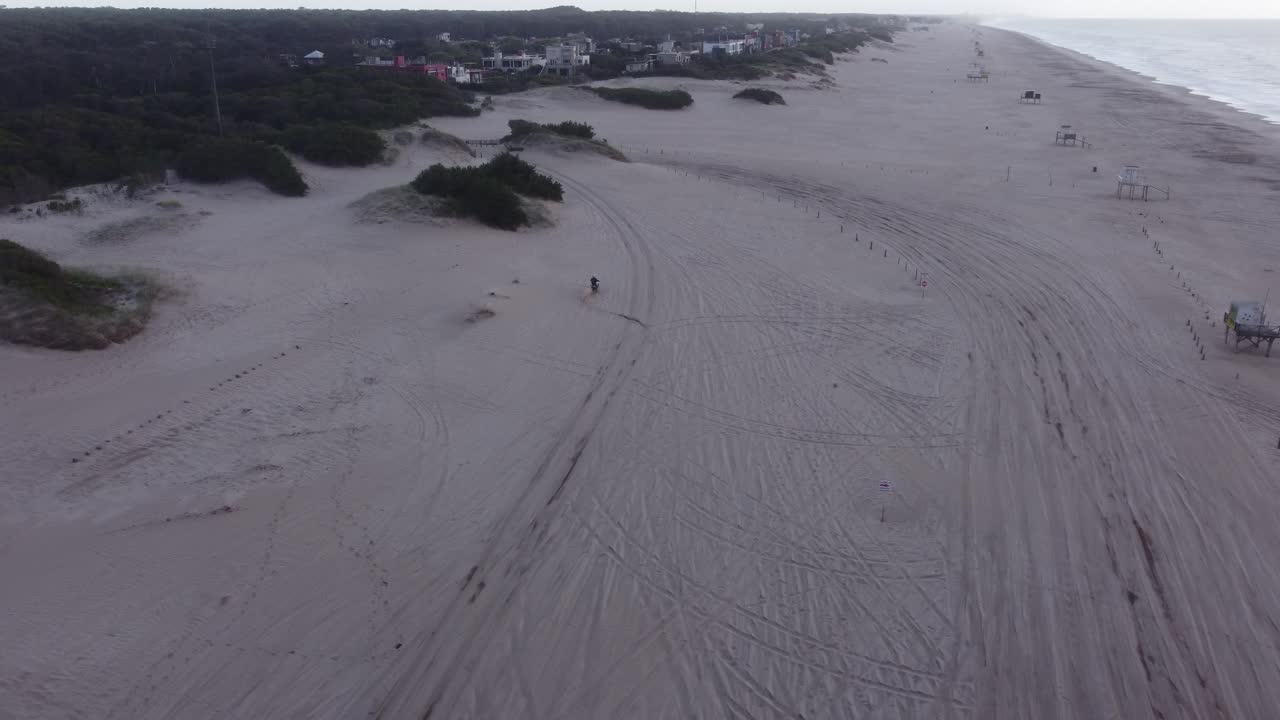 siguiente toma aérea de la conducción de motocicletas en la playa de arena durante el día nublado