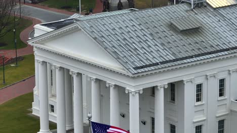 american and virginia flags waving in front of white columns of the capitol building in downtown richmond