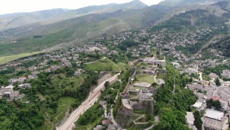 Drone-view-in-Albania-flying-in-Gjirokaster-town-over-a-medieval-castle-on-high-ground-fort-showing-the-brick-brown-roof-houses