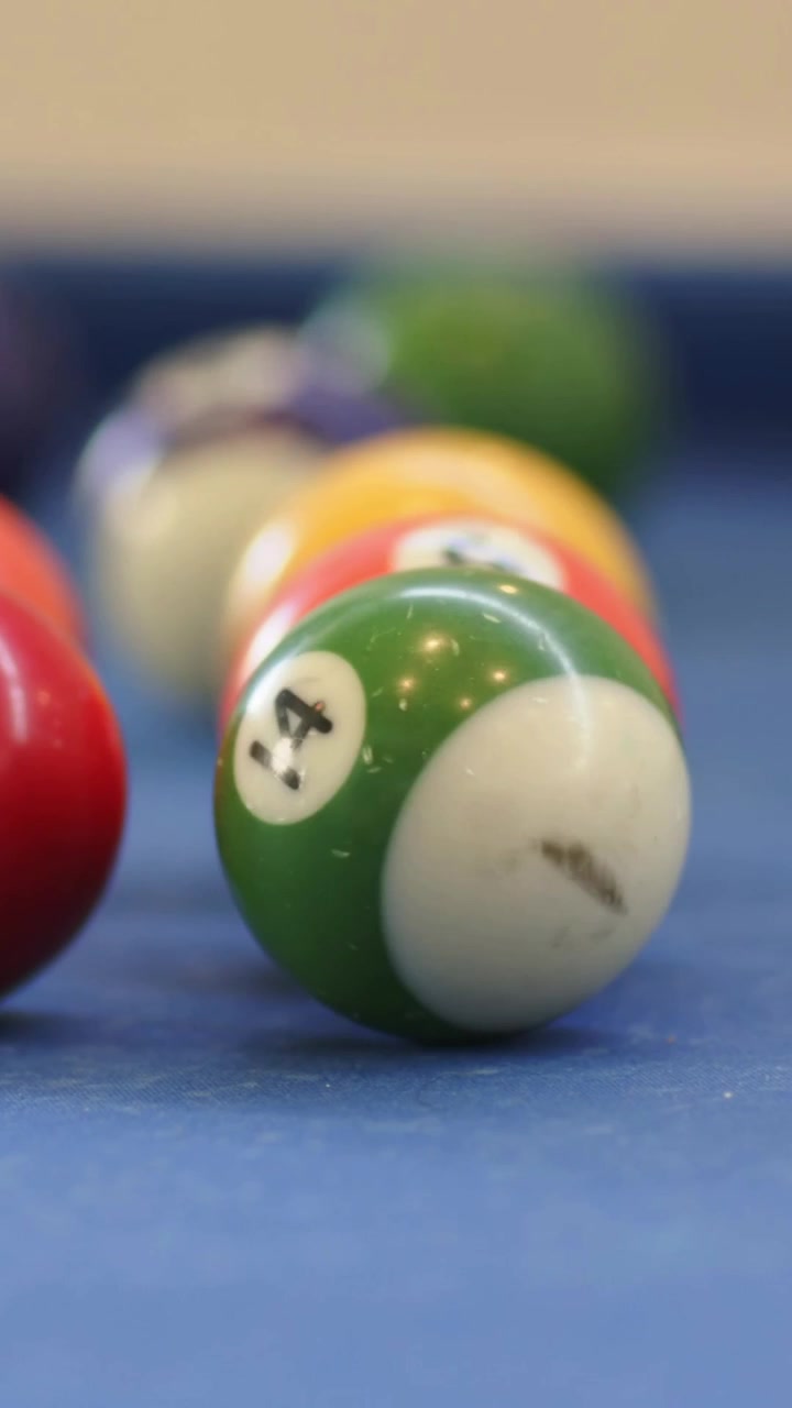 Vertical video: Pulling focus back, green 14 ball rotating on blue felt, red ball moving