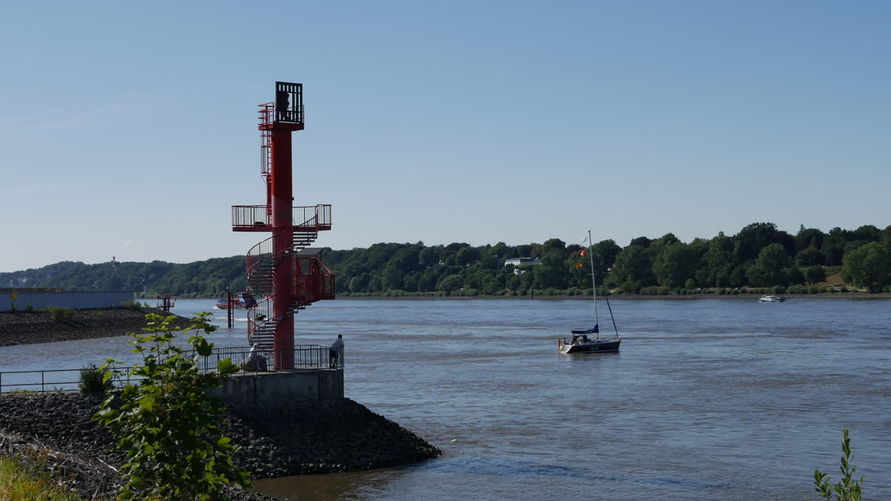 View point at Airbus Airport at southern banks of Elbe River at sunny day in Hamburg, Germany.Ships driving on the river. Some moving plants in blurry foreground.