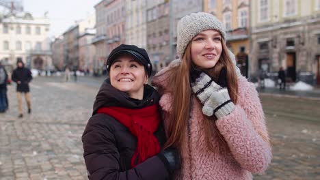 two smiling women tourists walking together on city street, family couple talking, embracing