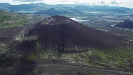 an aerial view of a large volcanic crater nestled within the mountains of iceland. the crater sits in a rugged, remote landscape surrounded by steep slopes and rocky terrain.