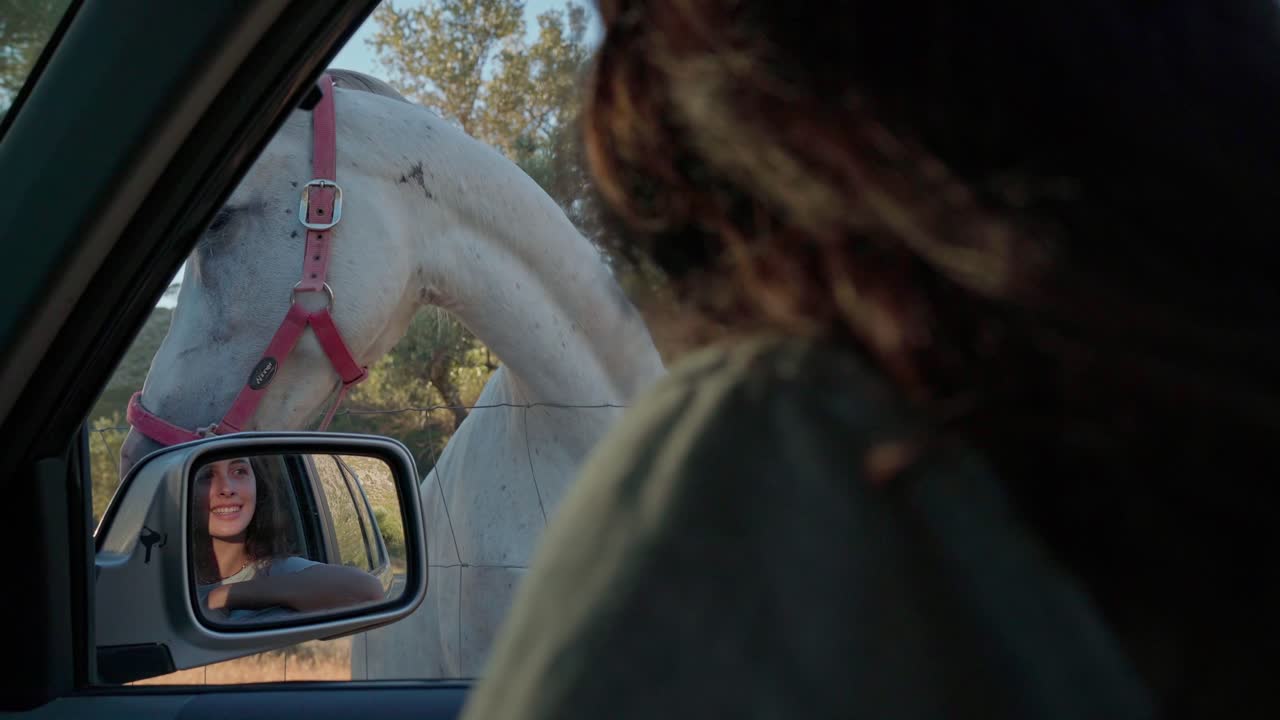 A Spanish girl leans out of her car window to greet a local horse in the scenic Serra de Tramuntana, with the stunning mountain landscape of Mallorca in the background.