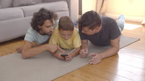 focused kid lying on floor near dads and using app