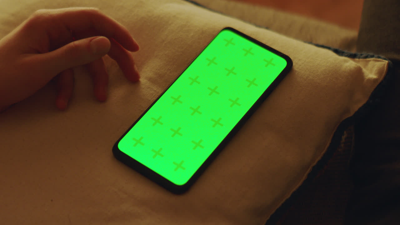 Mano che tiene un telefono con schermo verde su un cuscino