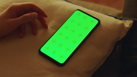hand holding phone with green screen on a pillow
