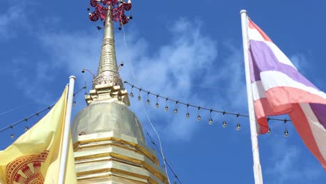 close-up of thai flags waving beside a golden stupa spire under a clear blue sky.