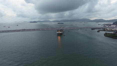 Puente-Colgante-Con-Un-Gran-Buque-Portacontenedores-Acercándose-Al-Fondo---Disparo-En-órbita-De-Drones