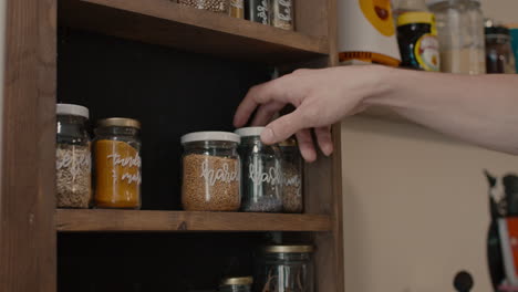 hand picking smoked paprika and poppy from wooden cruet shelf full of seasonings, spices and seeds in slowmo