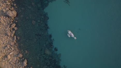 Drone-top-down-rising-above-boat-in-turquoise-green-sandy-water