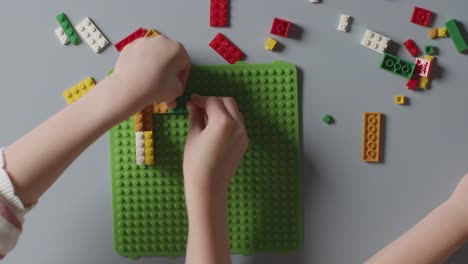 overhead shot of two children playing with plastic construction bricks on grey background 1