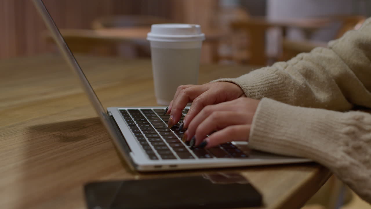 Push in on girls hands typing on laptop keyboard in cafe