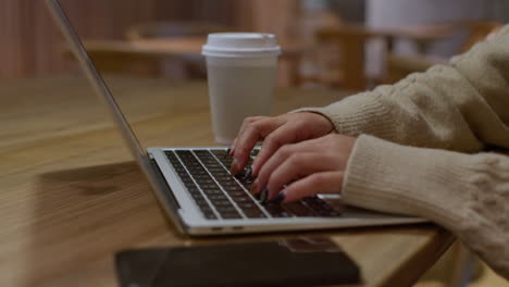 Push-in-on-girls-hands-typing-on-laptop-keyboard-in-cafe