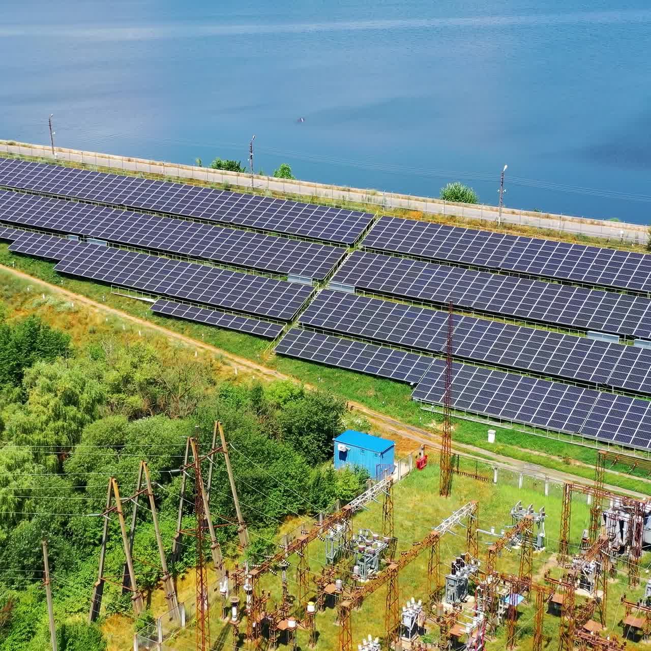 Solar power station in sunny day. Photovoltaic solar panels on blue water background. Electricity station on the bank of a river. View from above
