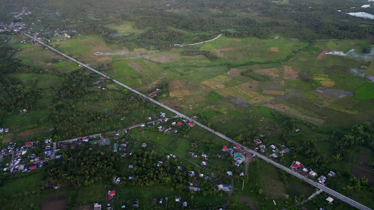 Stunning overhead drone shot of rural countryside highway road amid agricultural fields and villages during dusk - Catanduanes, Philippines.