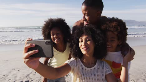 Padres-Afroamericanos-Y-Sus-Hijos-Tomándose-Un-Selfie-Con-Un-Teléfono-Inteligente-En-La-Playa