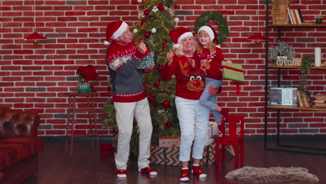 viejos abuelos alegres con la nieta niño bailando en casa cerca del árbol de navidad decorado