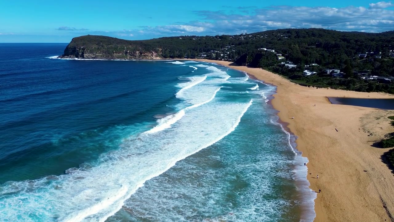 Drohnen-Luftaufnahme einer Küstenlandschaft mit Meereswellen, die an einem Sandstrand bei Copacabana brechen, mit dem MacMasters Headland und ländlichen Vorstädten im Hintergrund an der Central Coast NSW Australien Tourismus