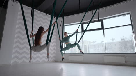 entrenador y mujer joven practicando gimnasia aero con suspensiones en el gimnasio. grupo de dos jóvenes mujeres hermosas yogi haciendo práctica de yoga aéreo en hamacas verdes en el club de fitness