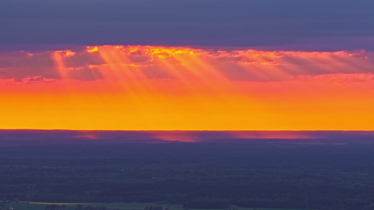 Sunbeams wander through dramatic clouds during a glowing orange timelapse sunset