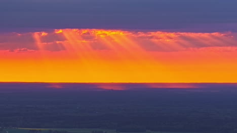sunbeams wander through dramatic clouds during a glowing orange timelapse sunset