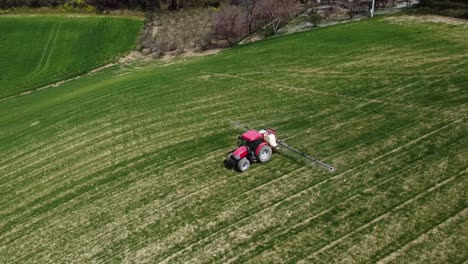 Aerial-view-of-farming-tractor-spraying-on-field-with-sprayer,-herbicides-and-pesticides-insecticide-to-the-green-field-plowed-land