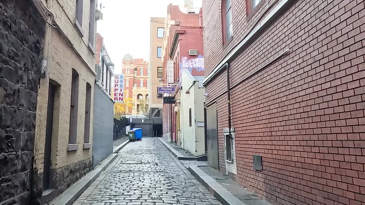 Explore a quiet, narrow alley lined with cobblestone and brick walls, leading to a vibrant urban scene.