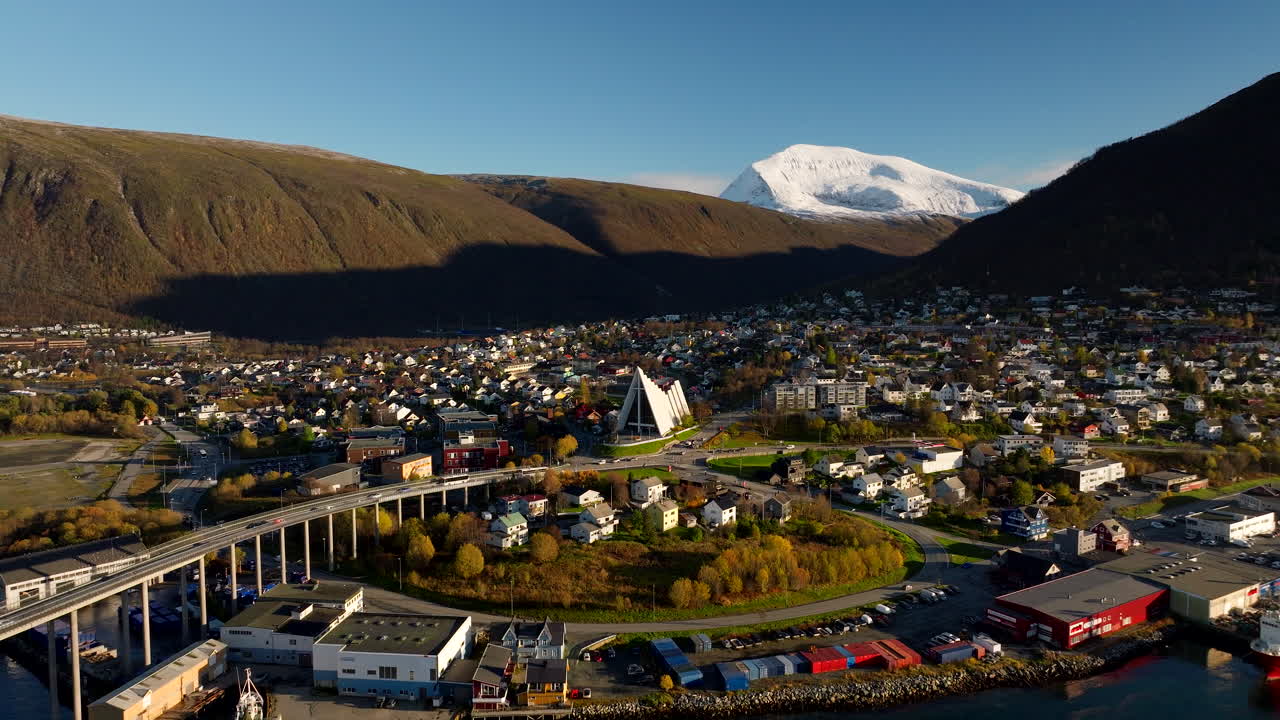 Drone pullback view of Arctic cathedral and Tromso bridge with traffic in fall
